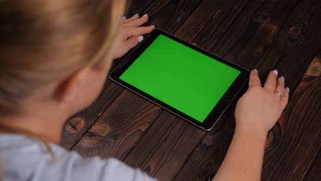 una mujer mira una pantalla de tableta verde sobre un fondo de madera.