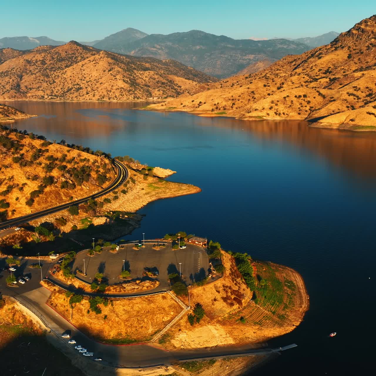 Amazing sunlit scenery of the lake surrounded by sloping rolled mountains. Drone approaching the parking lot and observation deck on the rock