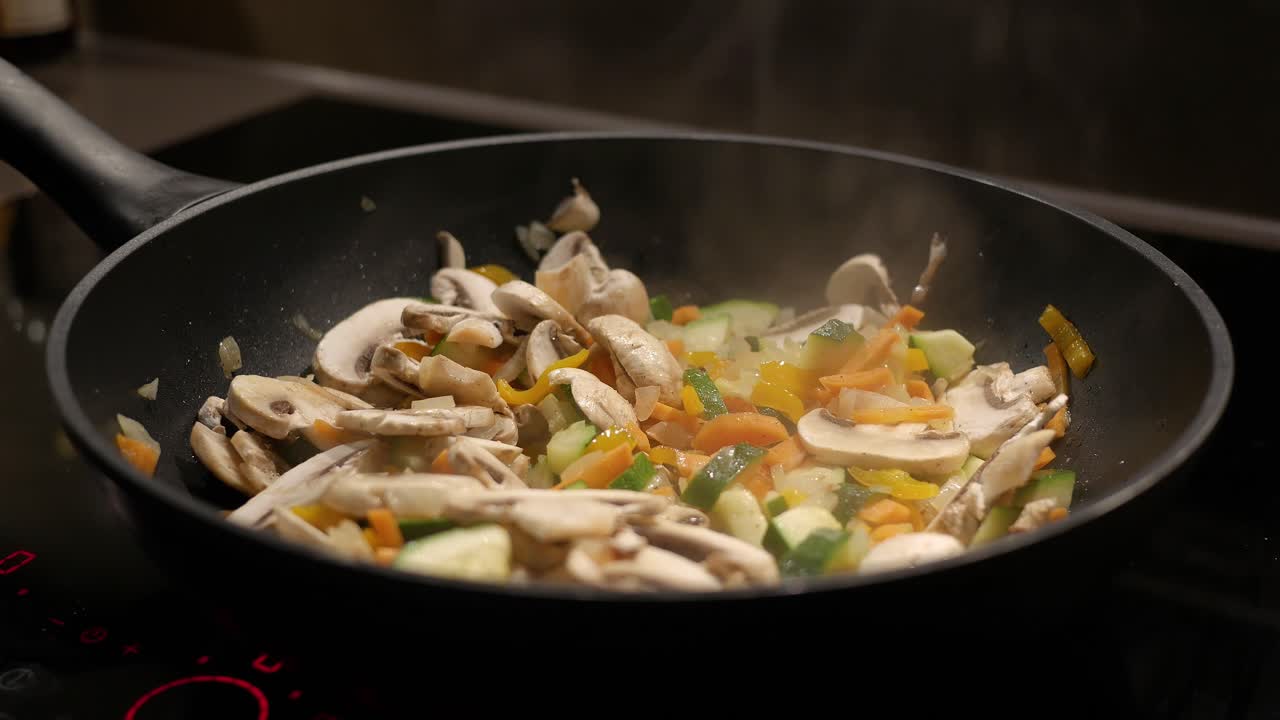 カメラの動きなしで、フライパンで油で炒められた細かく刻んだ玉ねぎ、にんじん、きのこ、その他の野菜