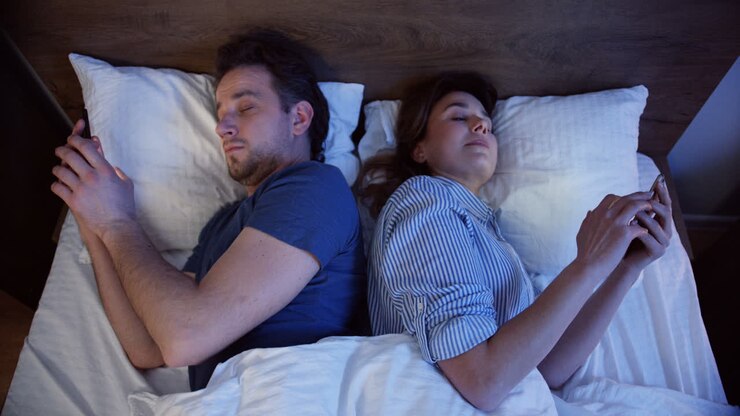 Top view of caucasian couple lying on the bed back to back and using smartphones at night, then they turn to each other for a second