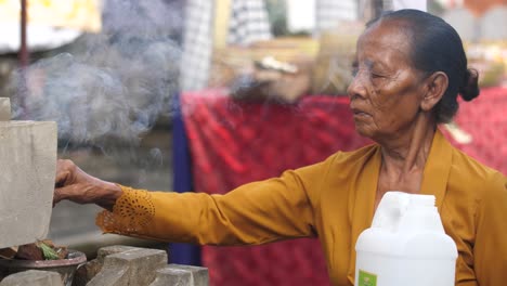 una anciana en bali tiende a hacer ofrendas y quemar incienso en su templo.