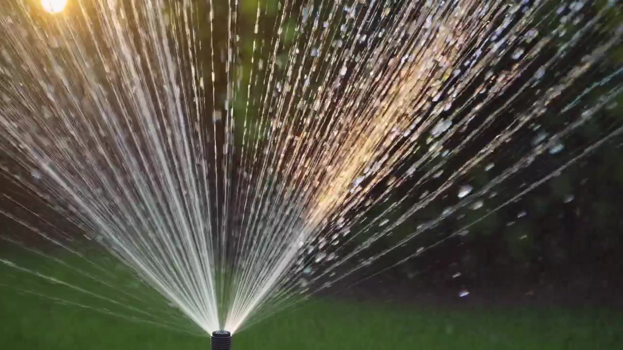 Irrigatore che spruzza acqua al rallentatore con la luce dorata del sole