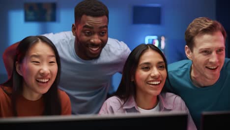 a group of friends gathering together to enjoy an exciting moment at their computer screens, sharing laughter and engagement in a vibrant and fun environment