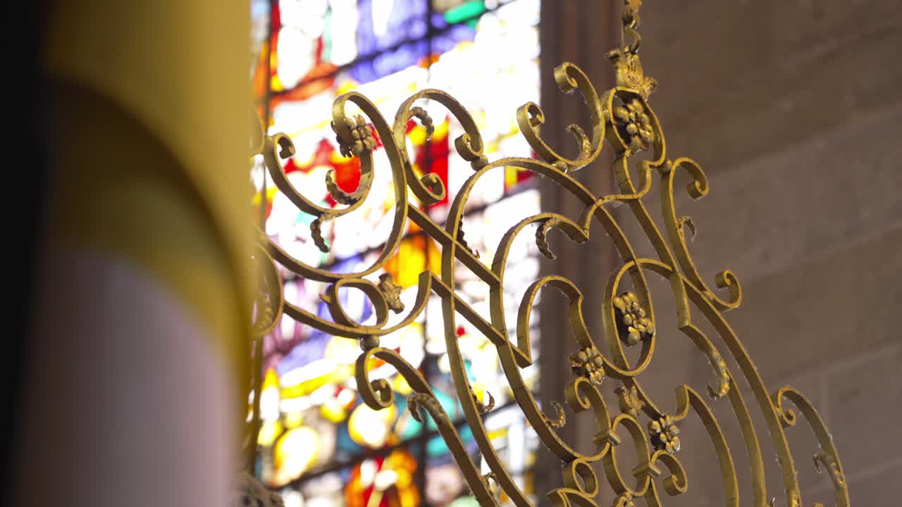 Close up of ornate golden wrought iron with colorful stained glass in the background