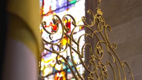 close up of ornate golden wrought iron with colorful stained glass in the background