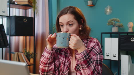 mujer bebiendo café y trabajando en una computadora portátil en casa