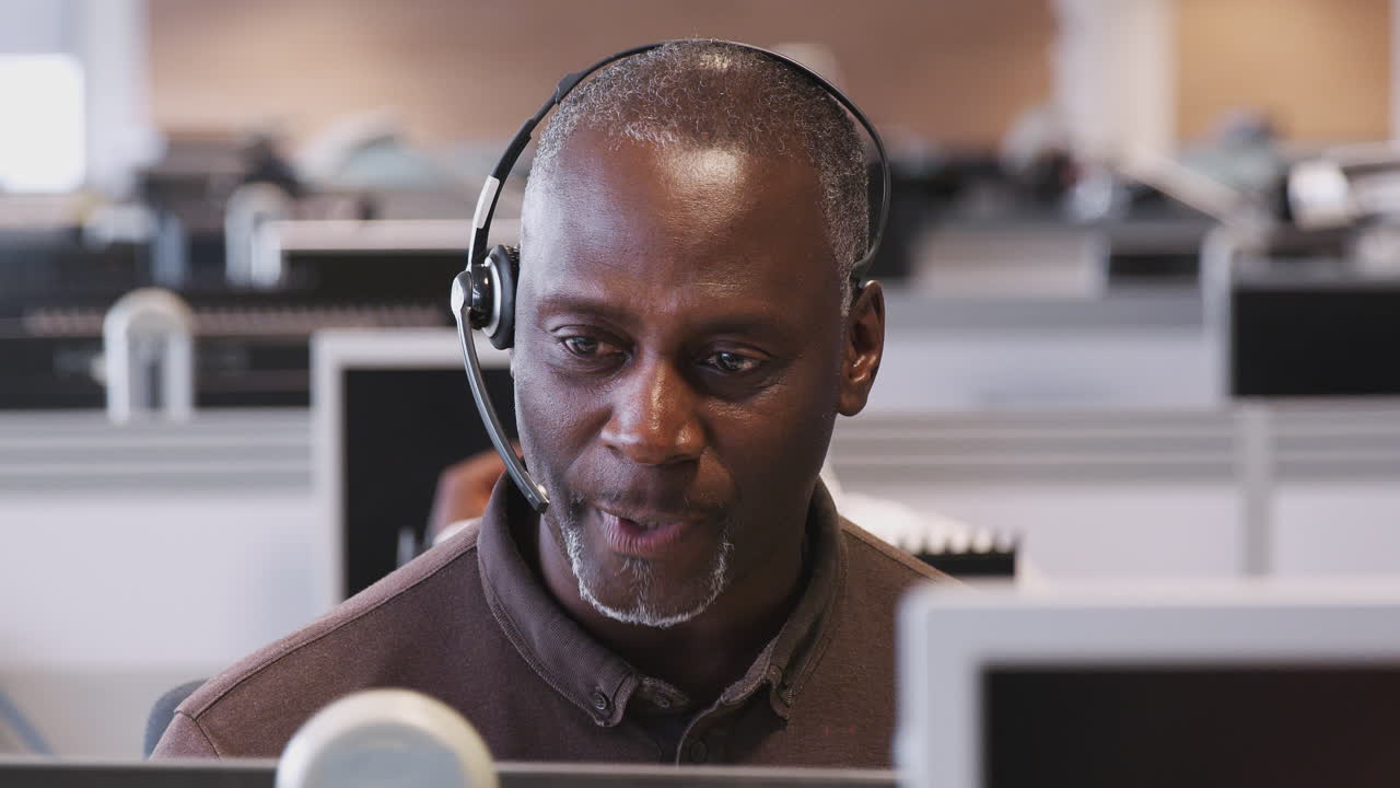Mature Businessman Wearing Telephone Headset Talking To Caller In Customer Services Department