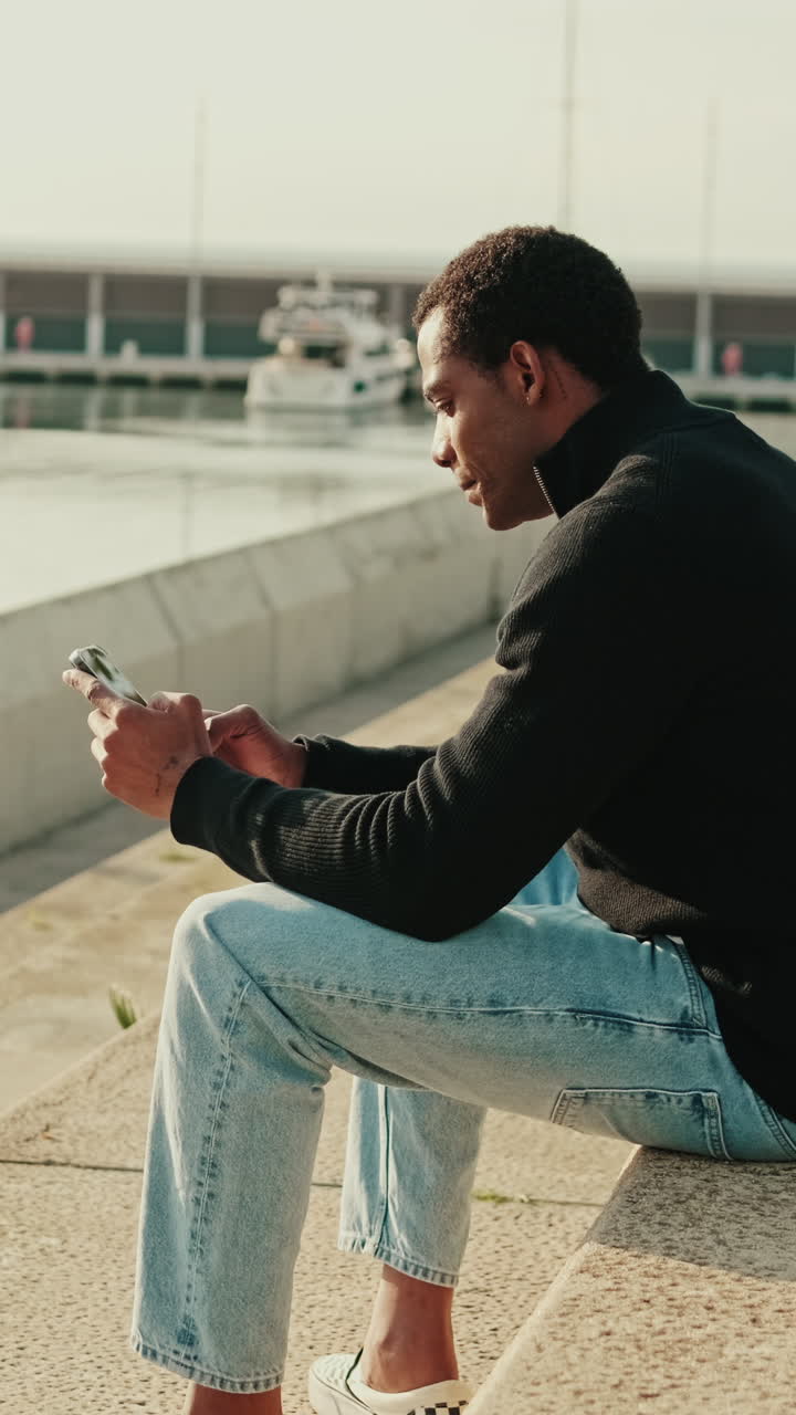Young Man Using Smartphone While Sitting by the Harbor