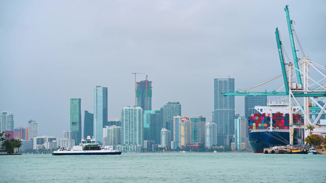 Miami harbor skyline with ferry and cargo ship. Miami bay view with ferry, PortMiami cranes, cargo ship, skyline, hazy sky, copy space.
