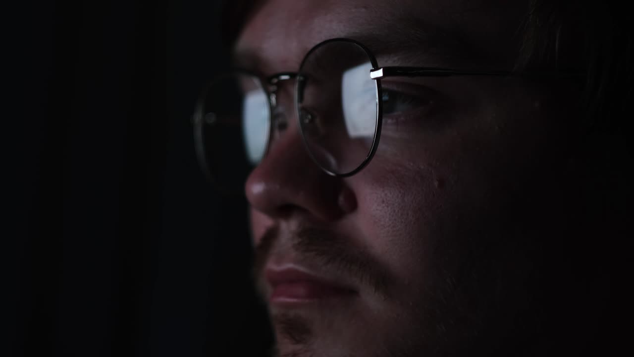 hombre con gafas, enfocado en algo con poca luz.