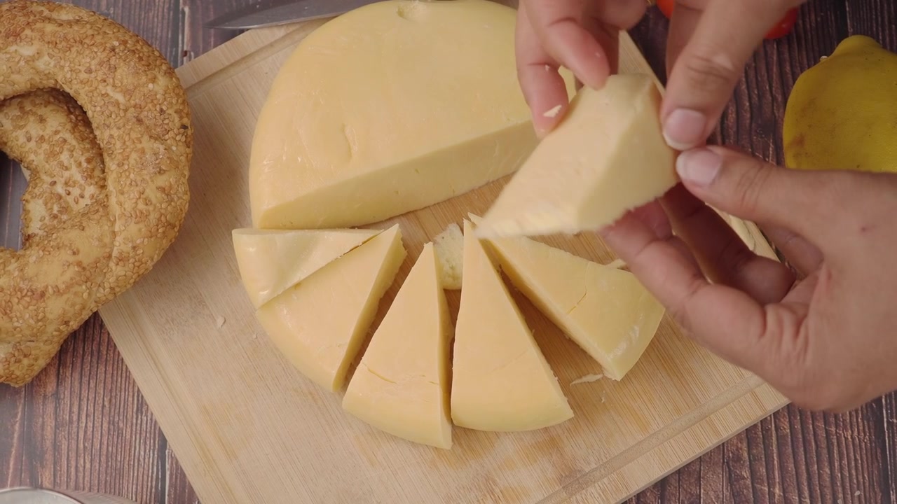 Mãos Cortando Fatias de Queijo Amarelo em uma Tábua de Madeira