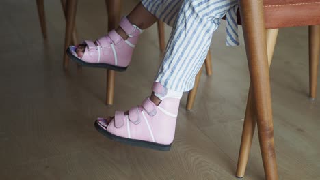 niño pequeño con zapatos ortopédicos rosados sentado en una silla