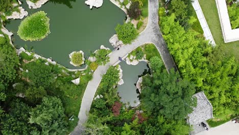 aerial bird's eye view with counterclockwise helix of a pond in a beautiful chinese garden on a sunny afternoon at huancui lou park, weihai city, china