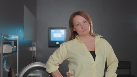 elegant laundry owner posing indoors beside open stainless washer in modern laundromat, hand on hip, confident entrepreneur showcasing clean facility, control panels glowing