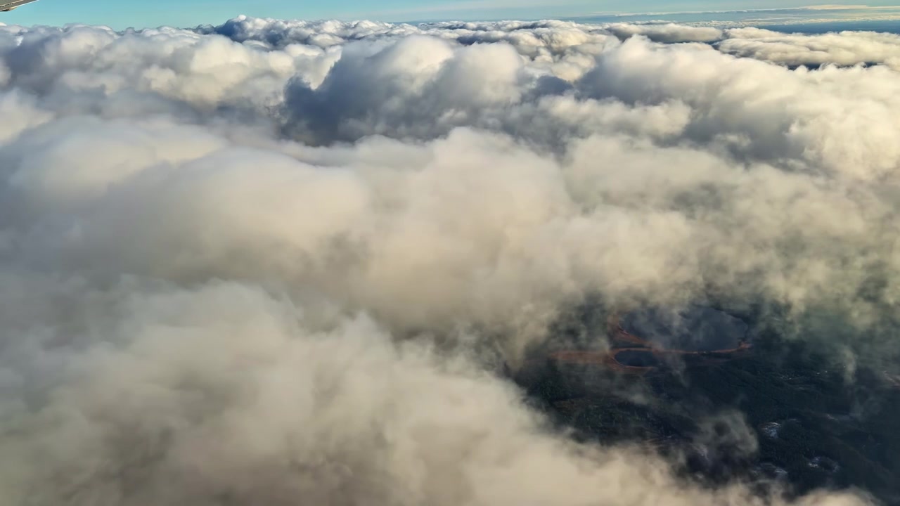 Airplane Window Static Shot Over Dramatic Cloud Layer Revealing Landscape Below, Symbolizing the Vastness of Baltic Skies Over Riga Latvia