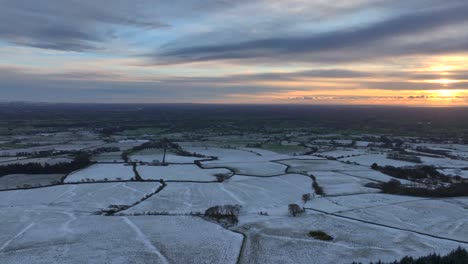 farmland fields dusted with snow fading out to green. slow pan revealing setting winter sun. lancashire, england, uk