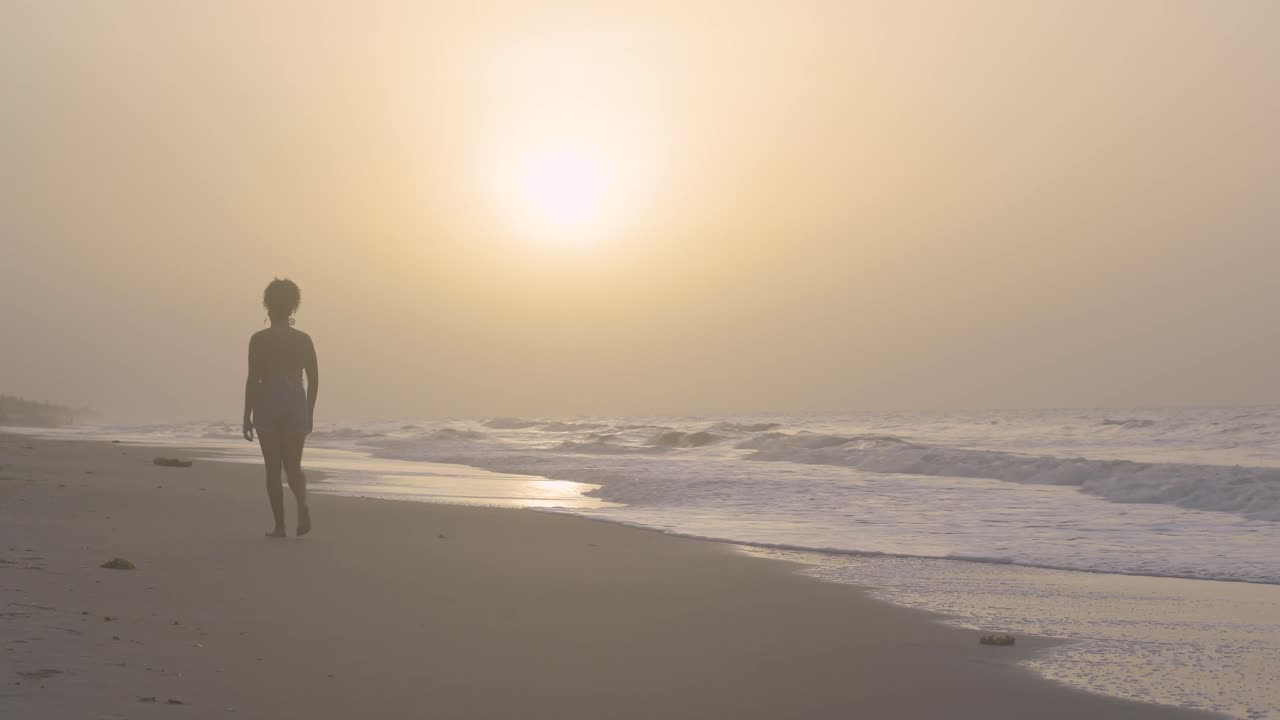 Young female walks on the seashore during sunset