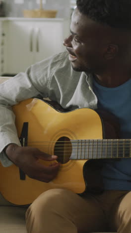 video of happy african american couple sitting on sofa, singing and playing guitar