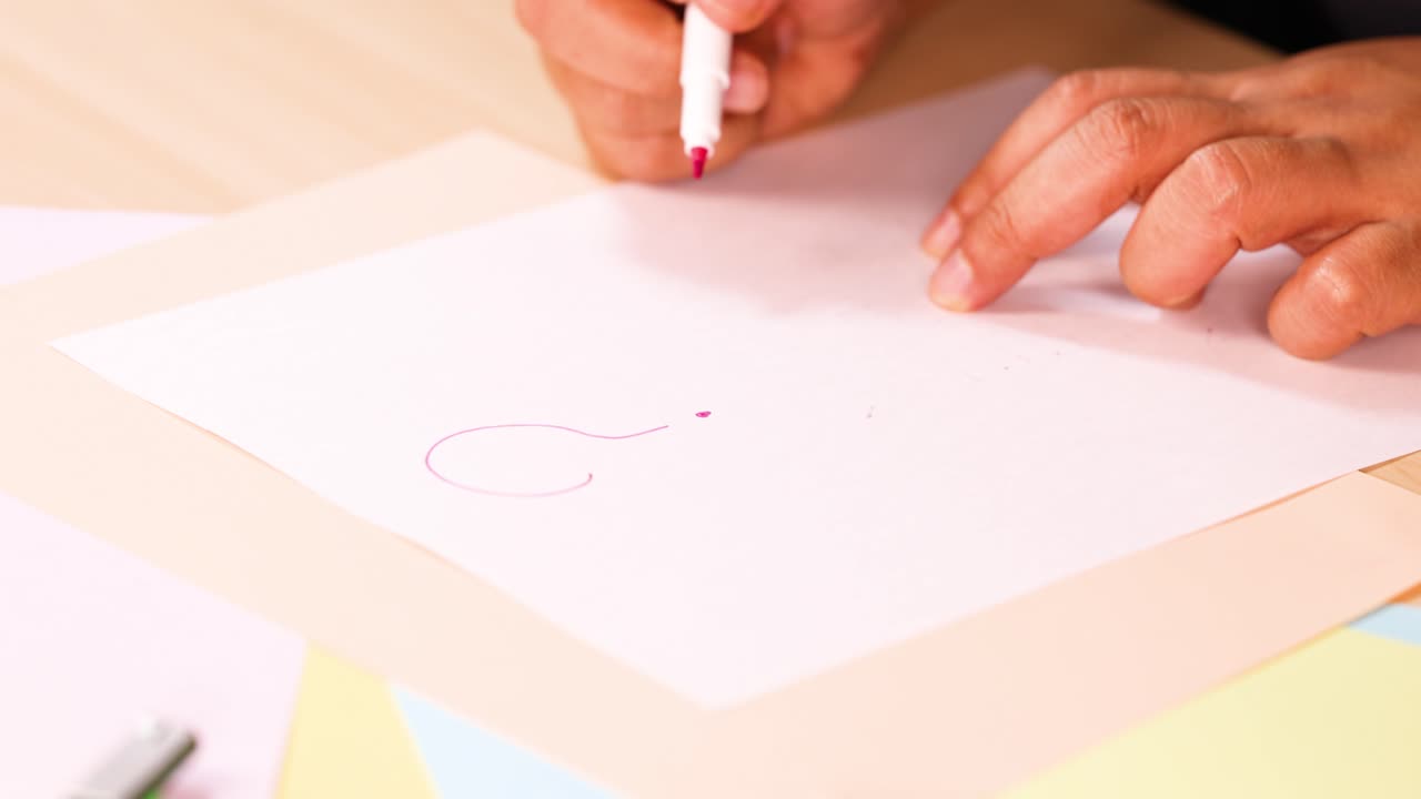Hand sketching a curved line on white paper with a red marker under bright lighting