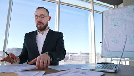 successful entrepreneur speaking in office. businessman in glasses and elegant suit sitting at the table in his workplace and talking seriously to someone.