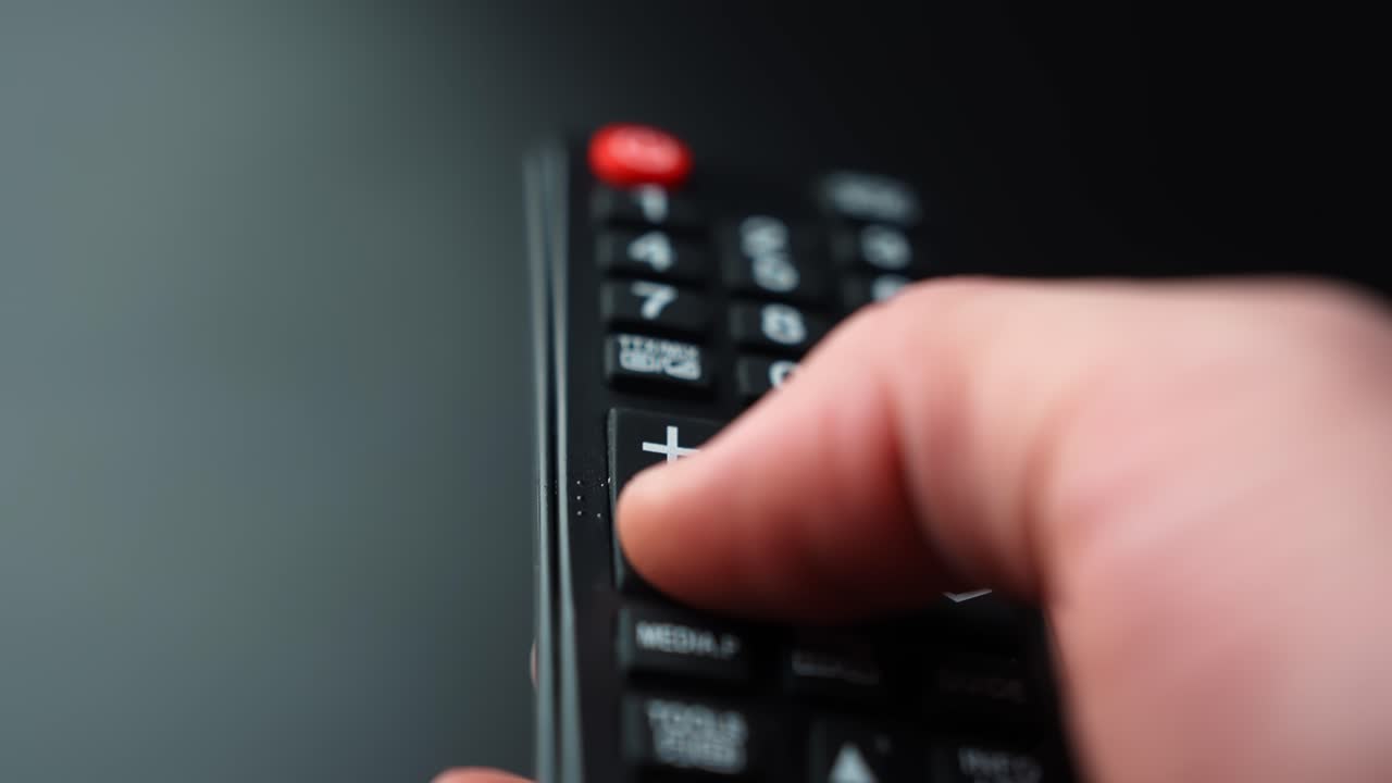 Nahaufnahme einer Hand, die die Leiser-Taste auf einer TV-Fernbedienung drückt, Lautstärke senkend mit geringer Schärfentiefe für Home Entertainment und Audio-Steuerung B-Roll