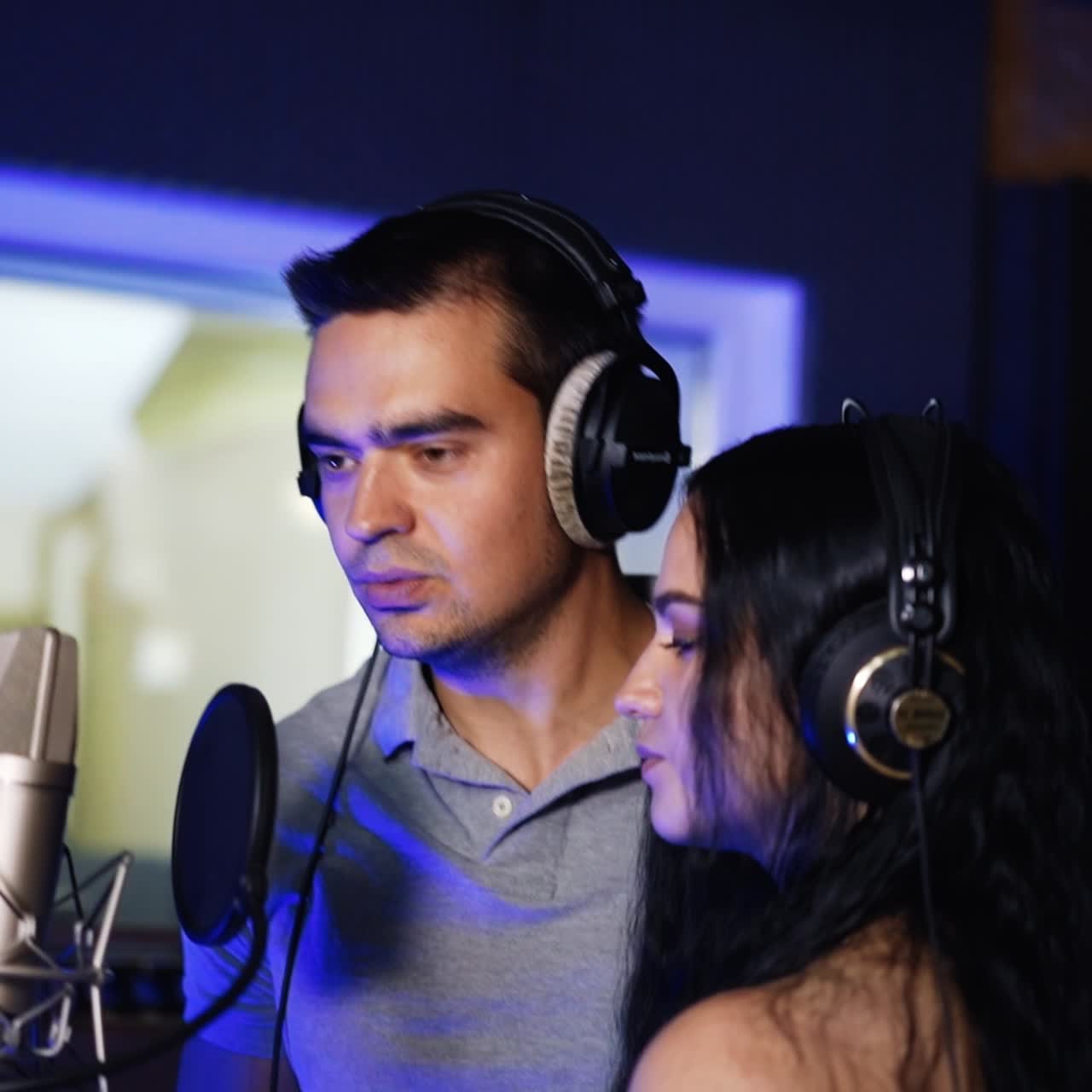 Duet performing a song in the professional studio. Man and woman wearing headphones singing and recording a song