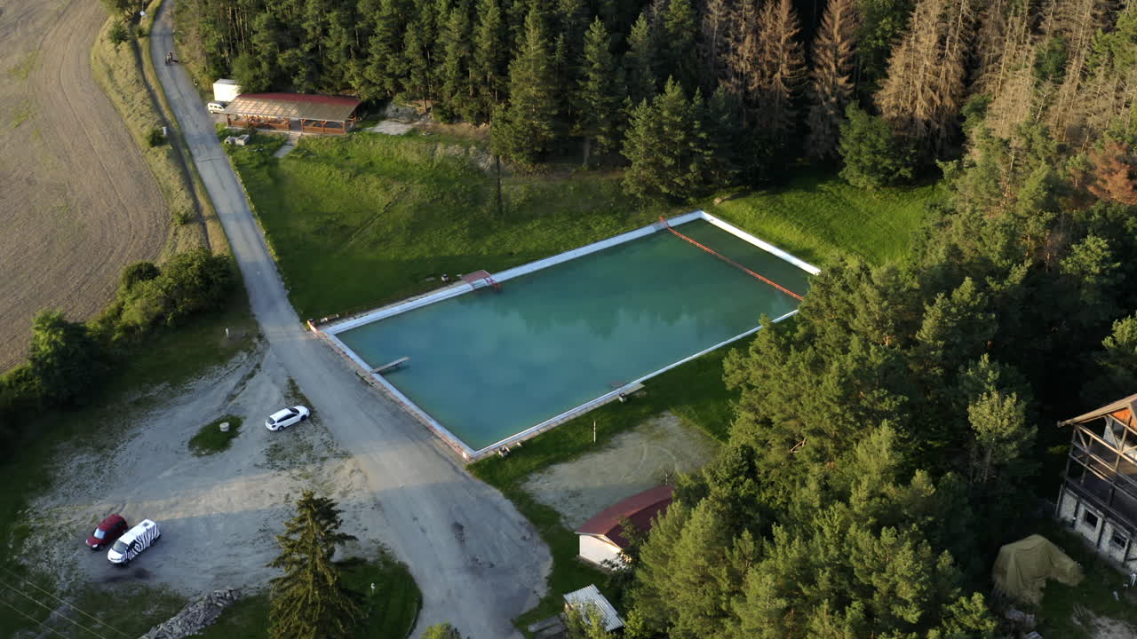 Luftfoto af luksuriøs udendørs swimmingpool og ruiner af en forladt ejendom i et landligt landskab.
