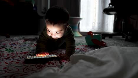 adorable bebé de 6 meses tendido en el suelo interactuando alegremente con la luz led rbg en el suelo en una habitación oscura