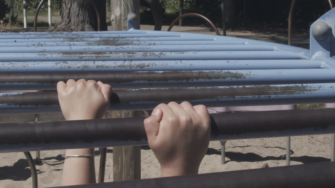 primer plano en cámara lenta de las manos de un niño mientras se cuelga de las barras de mono y luego se suelta