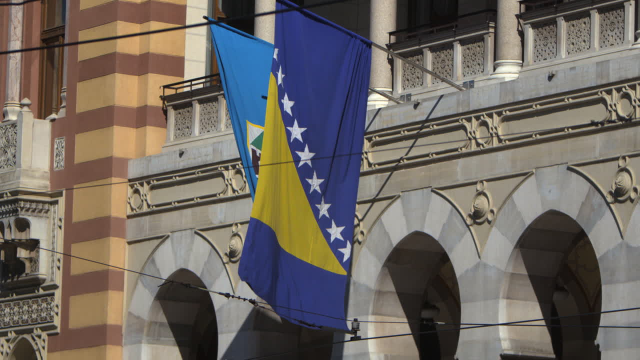 The Bosnia and Herzegovina flag is seen blowing in the wind during a cinematic slow motion shot at the Sarajevo capital building.