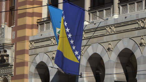 the bosnia and herzegovina flag is seen blowing in the wind during a cinematic slow motion shot at the sarajevo capital building.