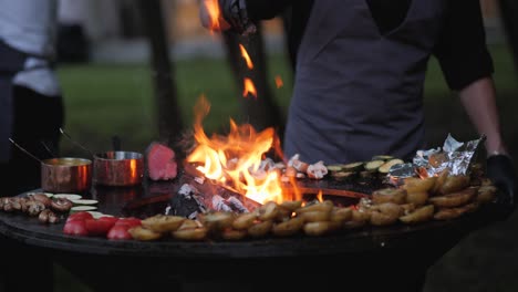 male chef preparing delicious grilled food on open fire grill in the backyard for the quests during summer evening