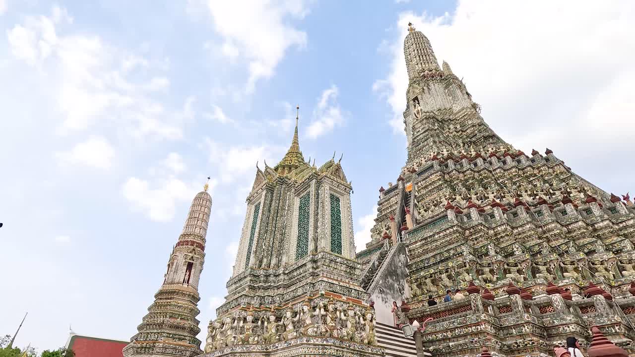 밝은 하늘 아래의 wat arun의 복잡한 건축물의 역동적인 시각, 장식 된 첨탑과 세부적인 공예품을 보여줍니다.