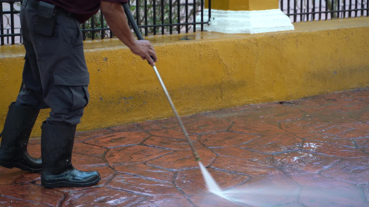 Closeup on waist down shot of person power washing the sidewalk pavement in a park