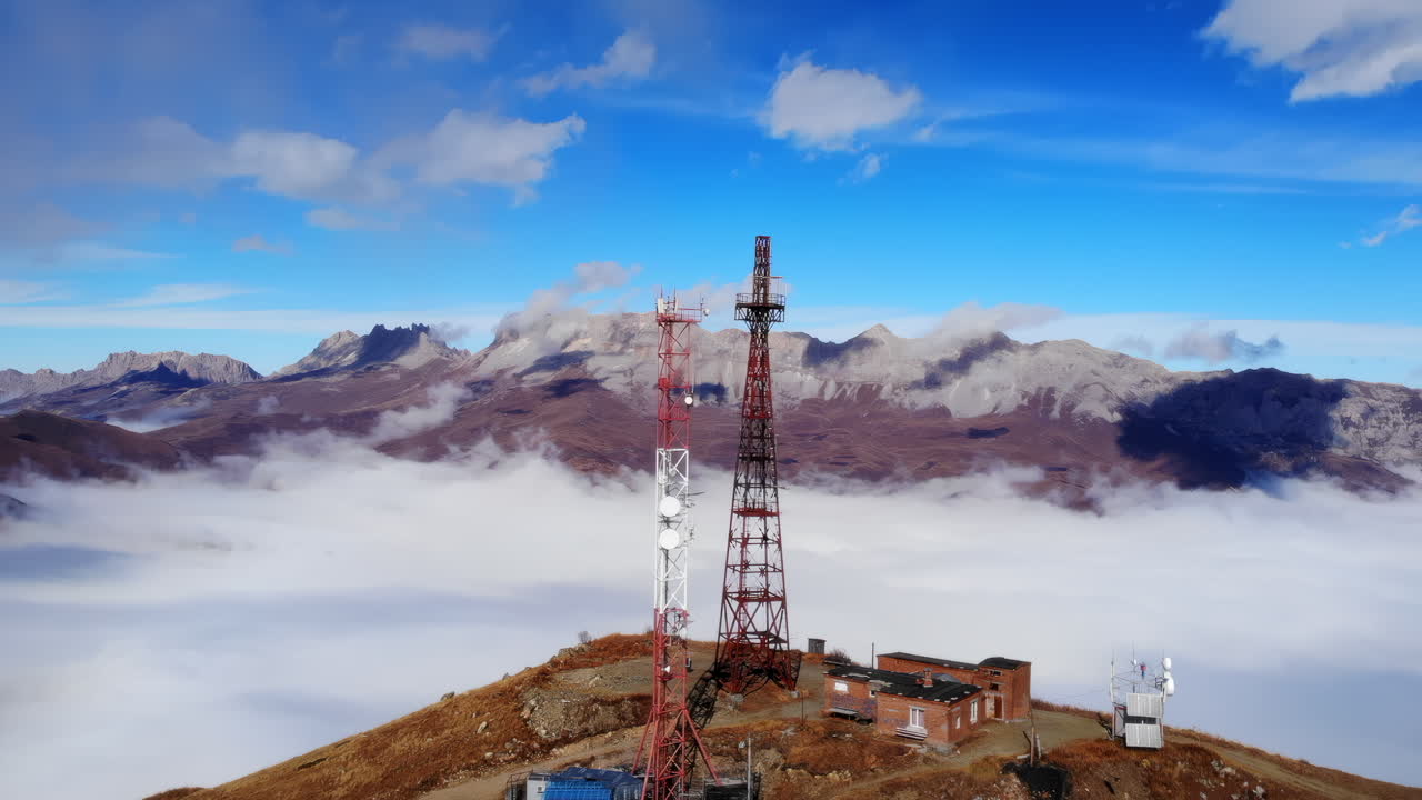 Complesso di torri di telecomunicazione sopra le nuvole, ampia vista aerea di torri a traliccio rosse accanto a edifici di manutenzione, mare.