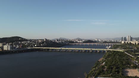 Aerial-drone-shot-flying-over-Han-River-in-Seoul-city-with-mountains-in-background,-South-Korea