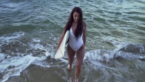 attractive young model walking on the beach towards the shore while holding surfboard - close up shot