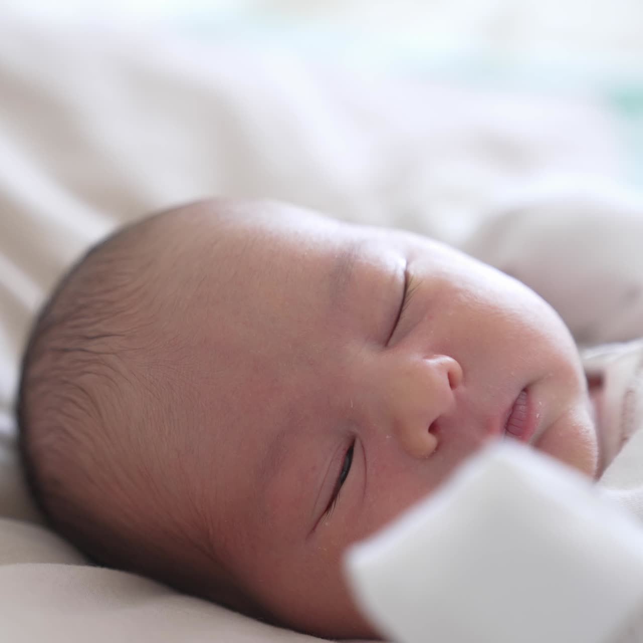 Un bambino piccolo sbatte lentamente le palpebre e si addormenta gradualmente. Un dolce bambino in vestiti bianchi su un letto bianco. Bellissimo viso di bambino in primo piano.