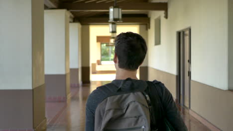 following behind a young caucasian male traveling alone with a backpack as he walks through a long empty corridor at a train station