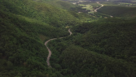 Aerial-view-of-countryside-road-passing-through-the-lush-greenery-and-foliage-tropical-rain-forest-mountain-landscape