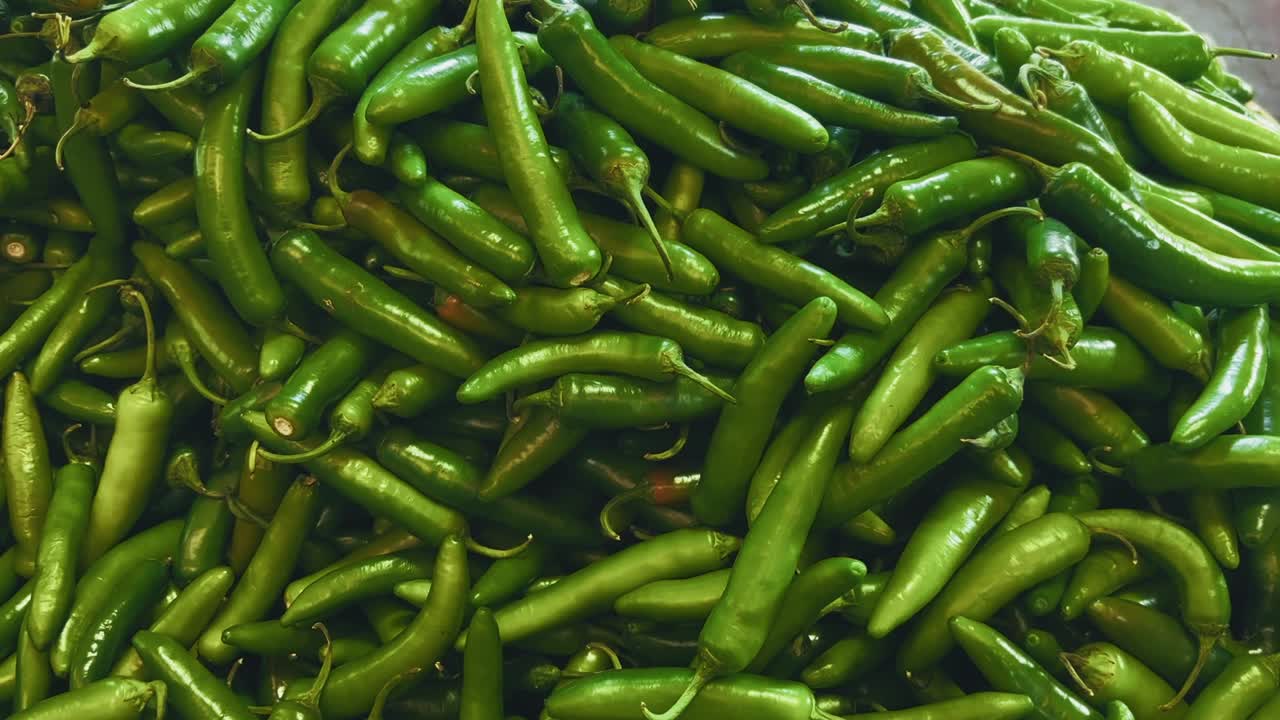Close-up of a large pile of fresh green chili peppers displayed for sale at a local market