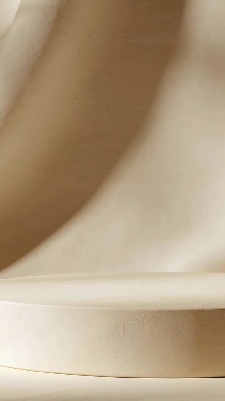 Video verticale: Illuminazione variabile che crea un piedistallo color crema e un drappeggio con un lento scorrere di ombre in studio.