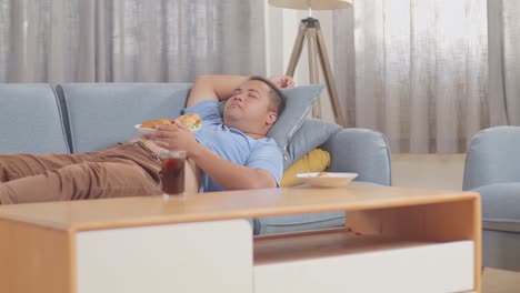 a fat asian man sleeping while having french fries with ketchup eating fast food on a sofa in the living room at home