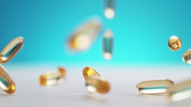 Yellow Fish Oil Softgel Capsules Fall Onto A Table And Bounce In Slow Motion and Macro, Blue Background