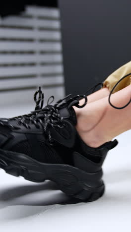 black trendy massive sneakers on female feet. woman wearing beige broad pants sits on the floor demonstrating her sport shoes. vertical video