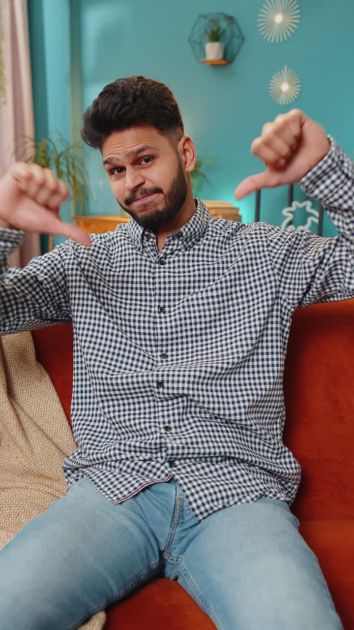 Upset Arabian man showing thumbs down, dislike bad work, disapproval dissatisfied feedback at home