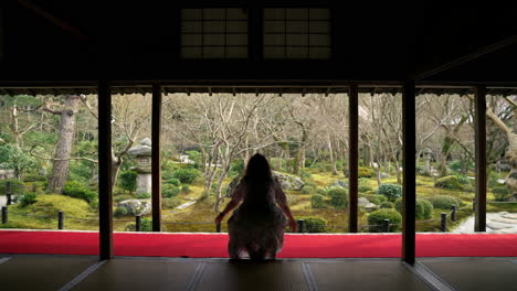 woman at enkoji temple walks and sit to meditate facing garden in kyoto, japan