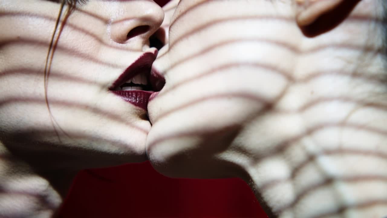 Due donne si baciano in studio, con il viso di destra inclinato e ombre striate.