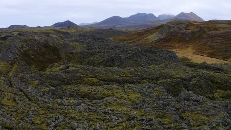 Icelandic-mossy-rocky-barren-volcanic-extreme-terrain-with-idyllic-mountain-range-skyline,-Aerial-view