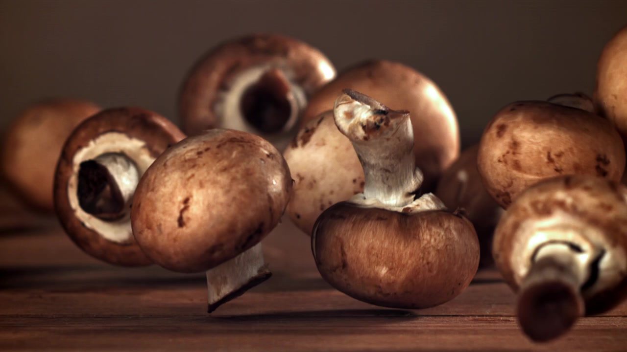 Brune champignoner falder ned på et træbord i slowmotion